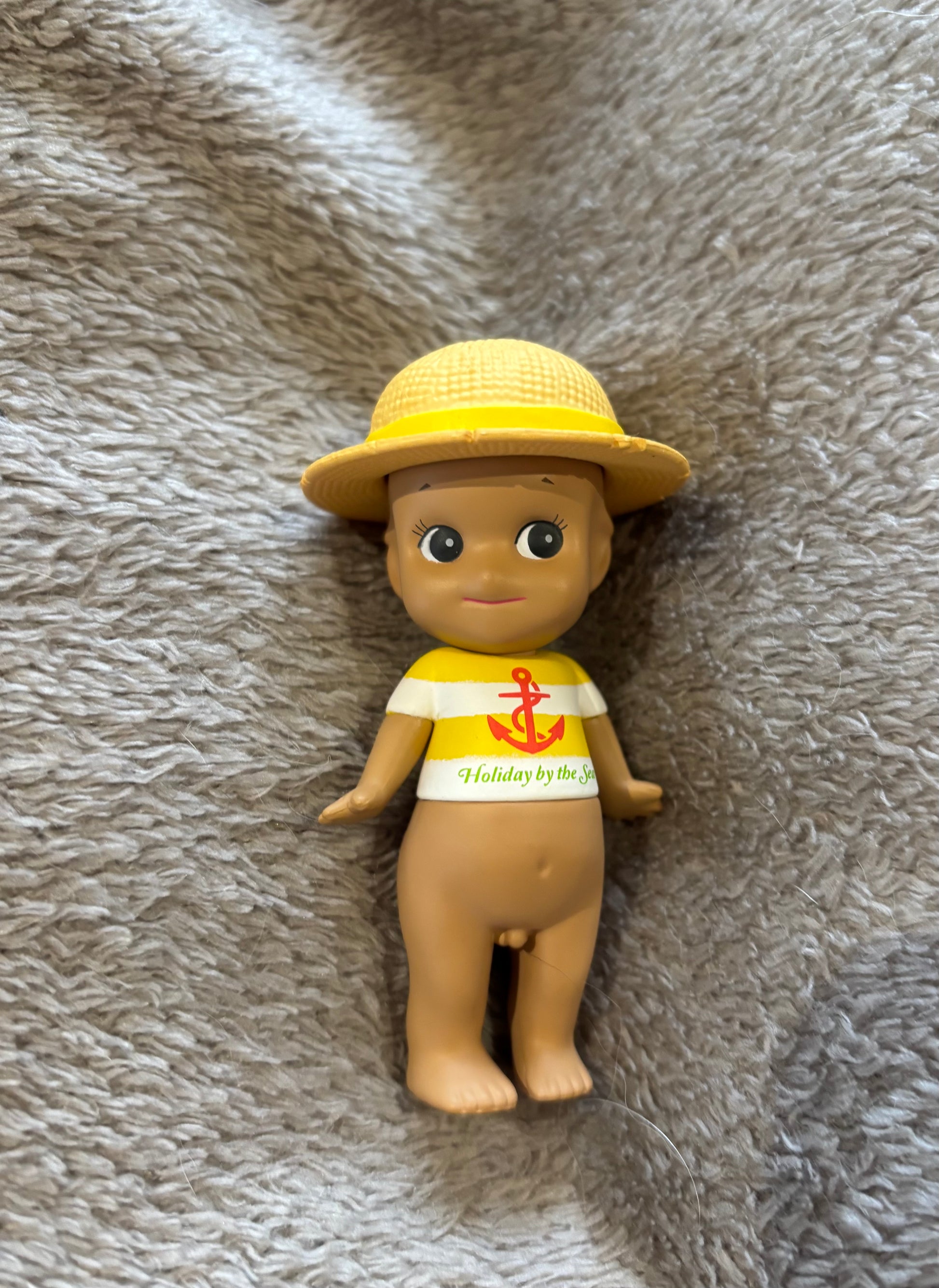 Cute rare Mini figure Sonny Angel Tan Hat Yellow Anchor Kewpie doll lying on grey blanket 
