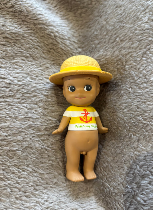Cute rare Mini figure Sonny Angel Tan Hat Yellow Anchor Kewpie doll lying on grey blanket 