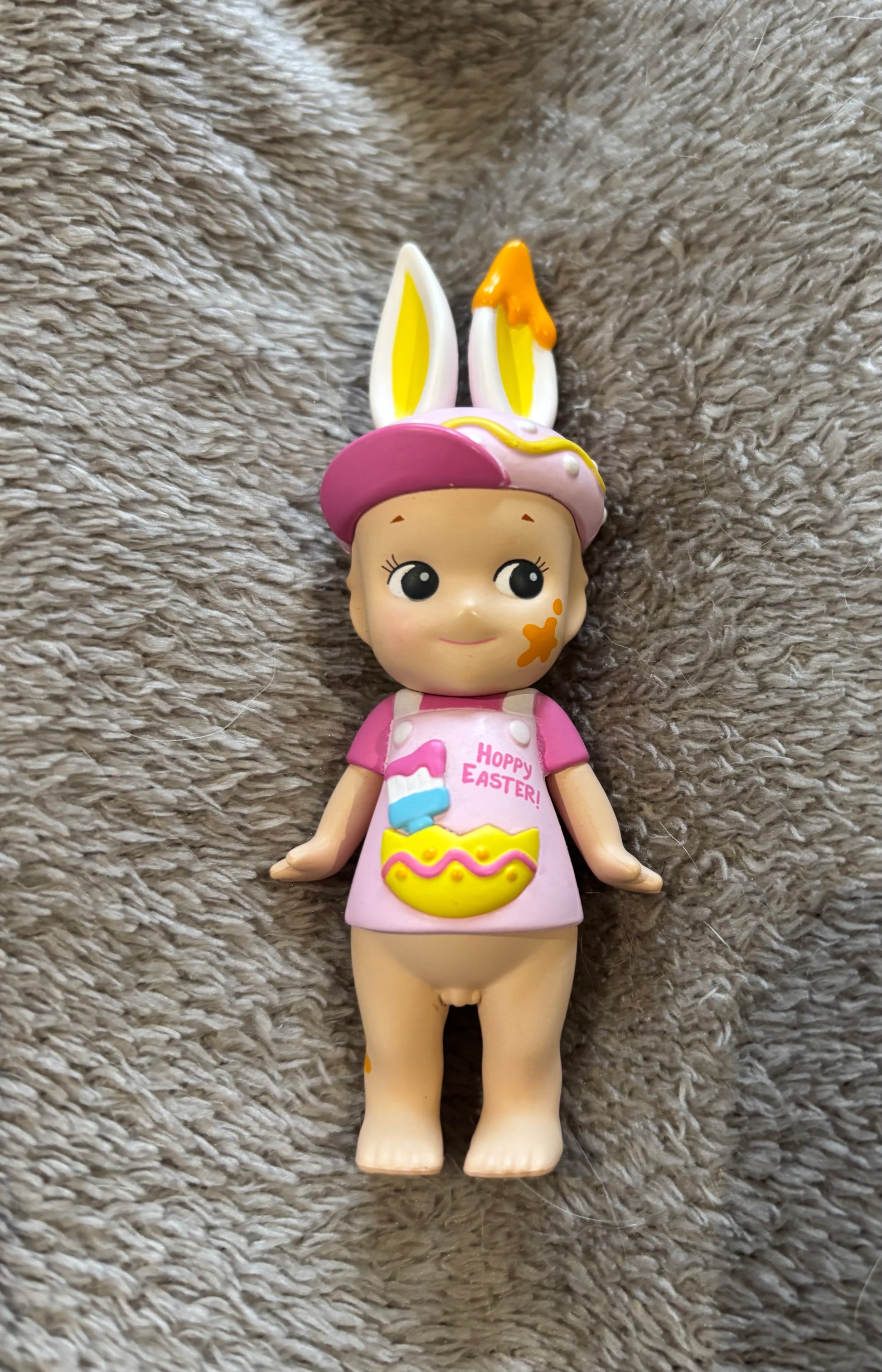 Cute rare Sonny Angel Rabbit Bunny Pink mini figure with paint splatter lying on grey blanket 