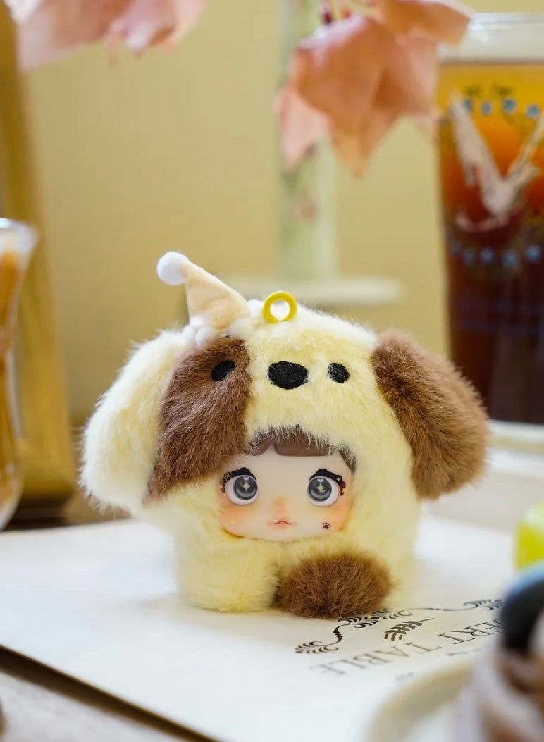 Plush nommi bag charm blind box collectible with doll face and puppy body on a table with a blurred background
