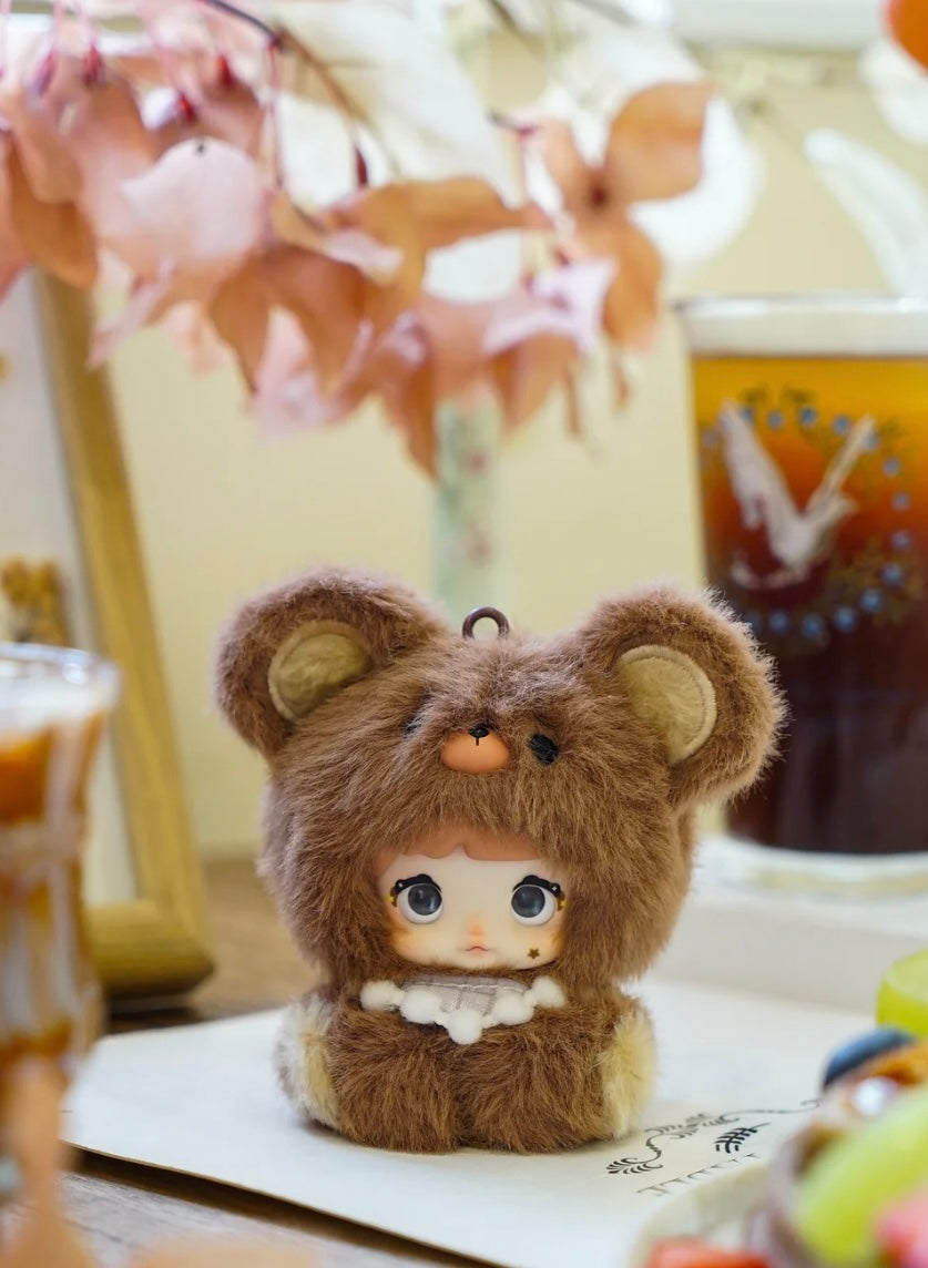 Small plush nommi  baby V1 toy with bear ears on a desk with a blurred background